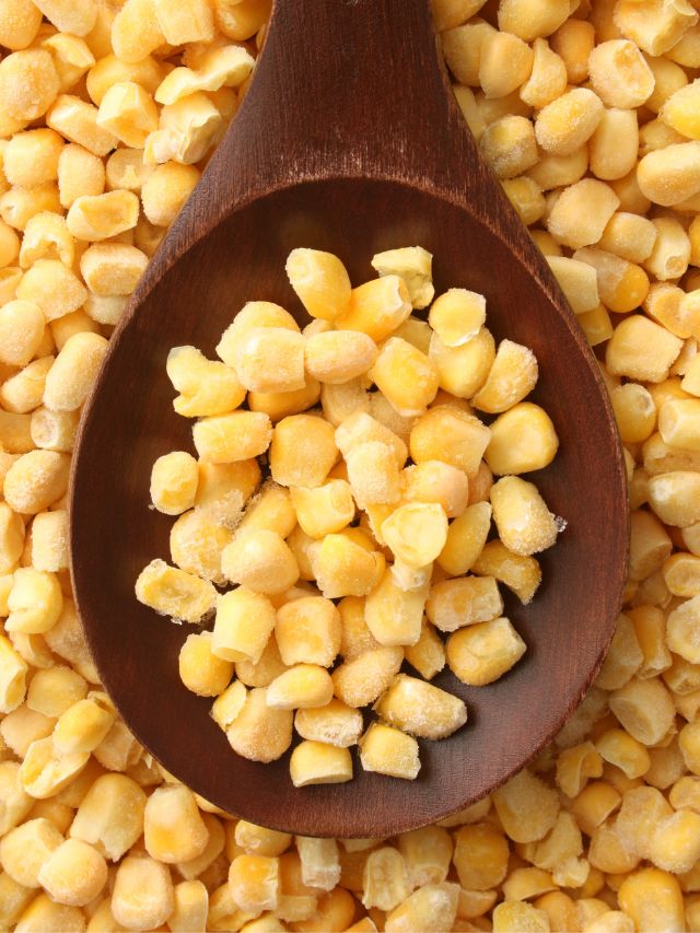 a wooden spoon full of frozen corn on top of frozen corn