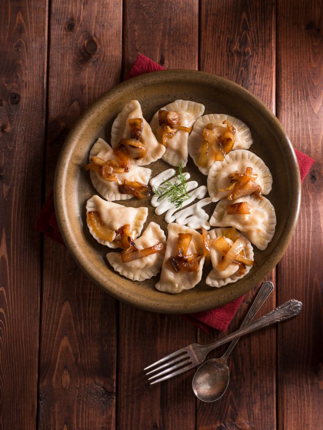 pierogies on plate with onions and sour cream on wooden table