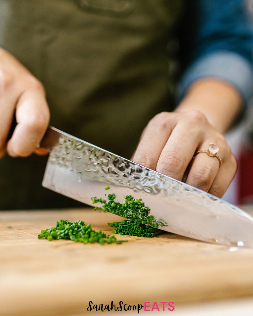 a person cutting chives on a cutting board with a japanese knife