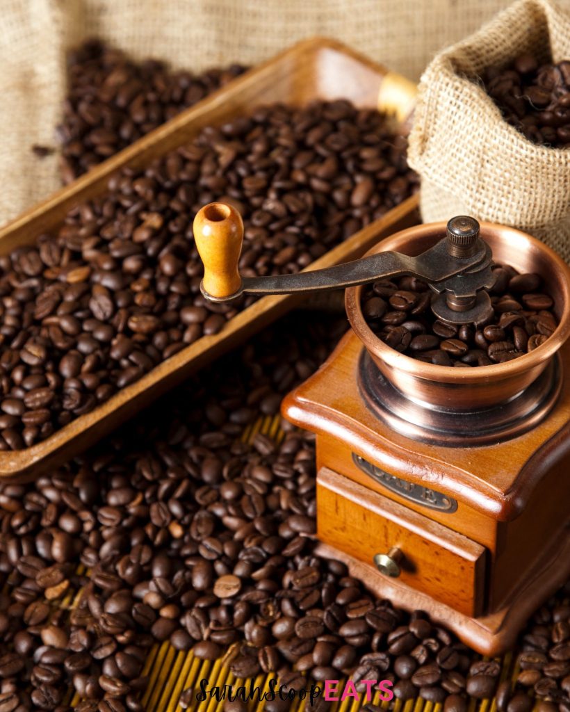 A coffee grinder and coffee beans on a sack.