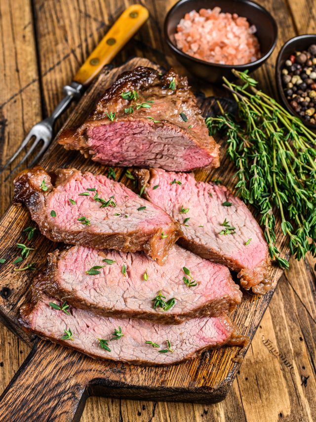 Steak on a wooden cutting board with herbs and spices.
