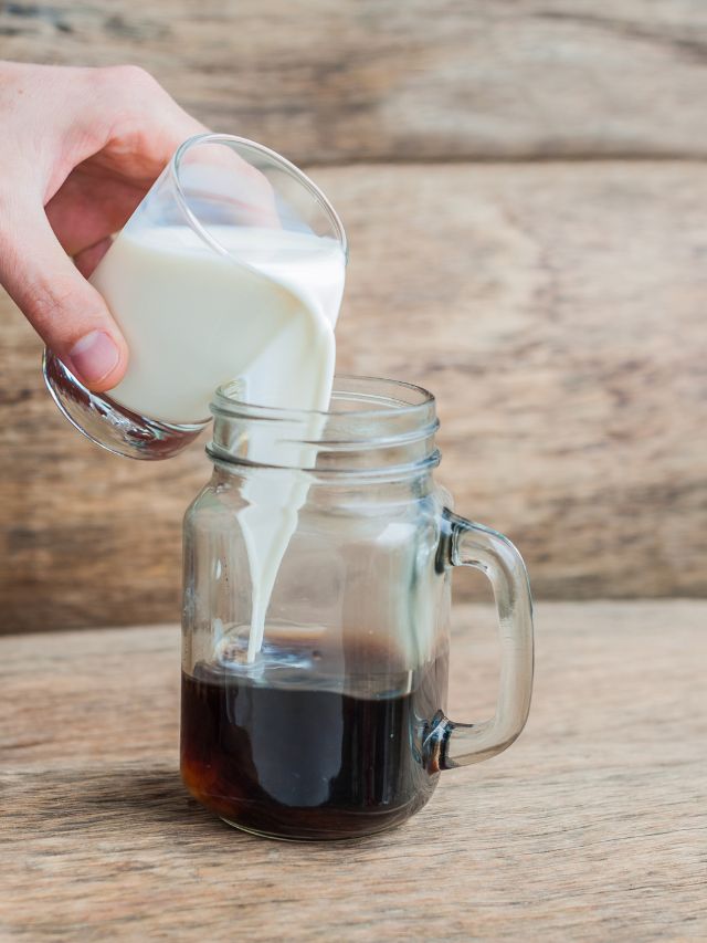 creamer being poured into half glass of coffee