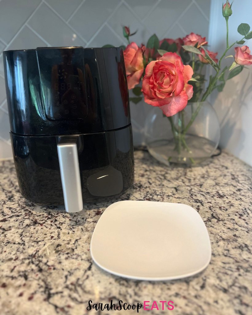 an air fryer, plate, and flowers on counter
