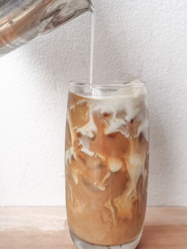 iced coffee in mug with milk being poured in