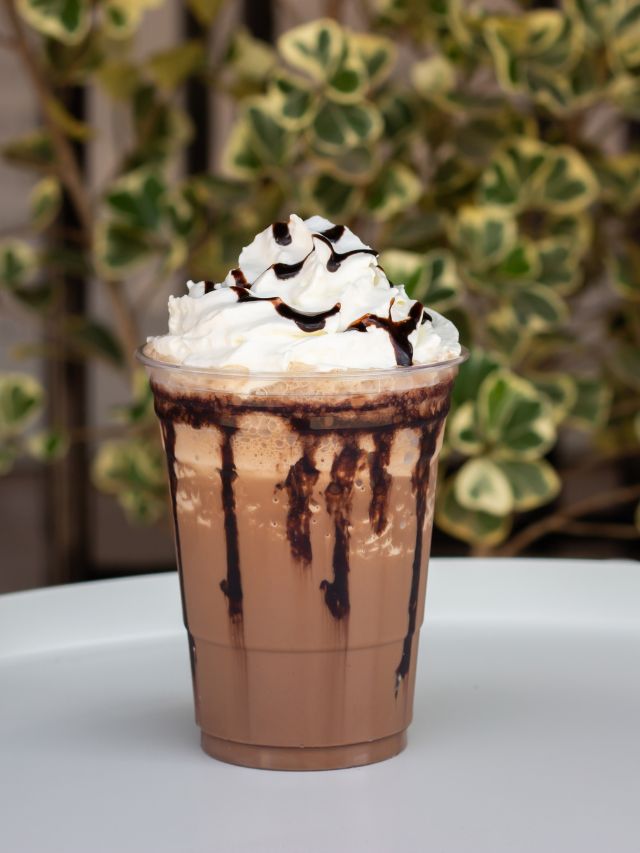 iced coffee mocha in cup outside with whipped cream and chocolate syrup
