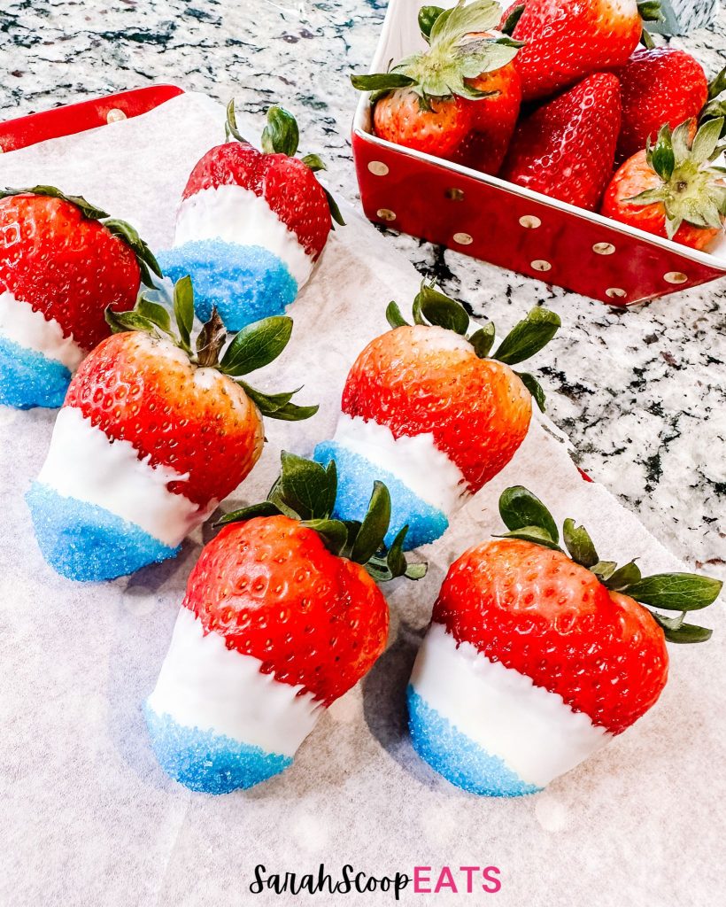 a tray of red white and blue chocolate covered strawberries by a red and gold bowl of strawberries