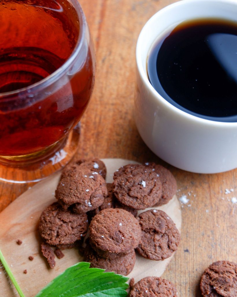 a cup of coffee and a cup of tea by a plate of cookies