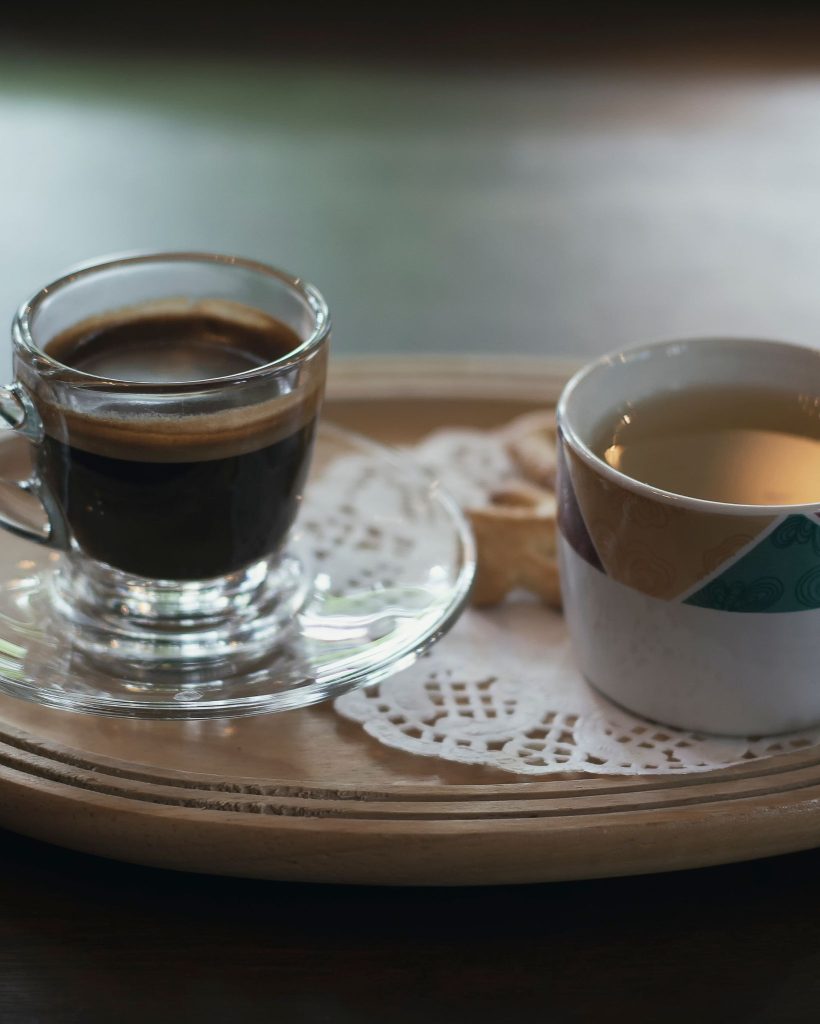 a clear cup of coffee on a plate next to a cup of tea