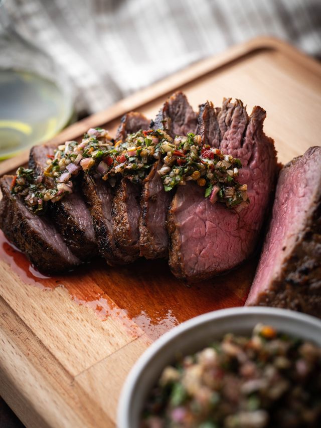 steak sliced on wooden cutting board with topping