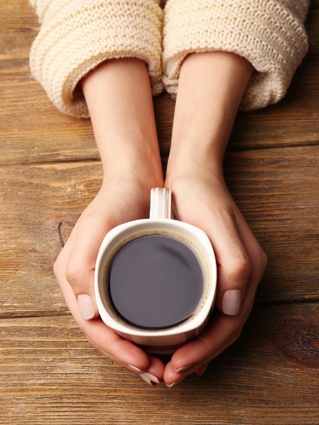 A woman's hands holding a cup of coffee on a wooden table.