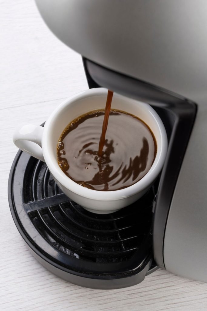 A cup of coffee is being poured into a coffee maker.