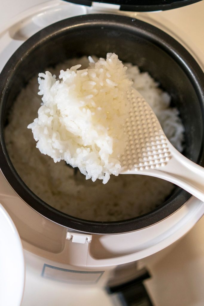 A spoon is being used to scoop rice out of a rice cooker.