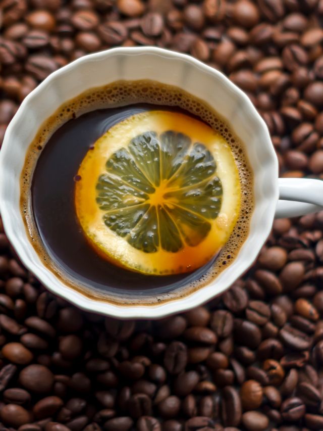 cup of coffee with lemon in it and coffee beans around it