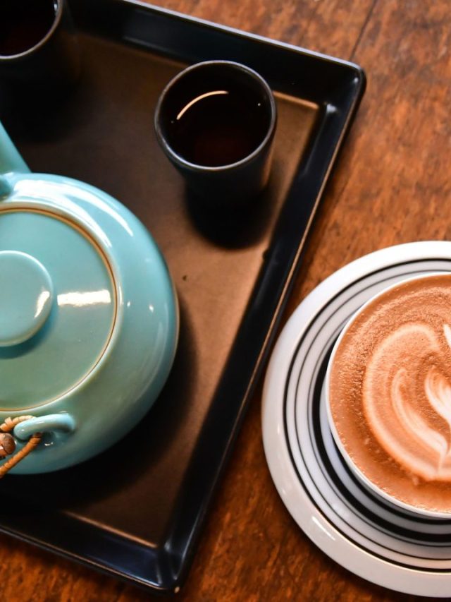 A cup of coffee on a tray next to a teapot.