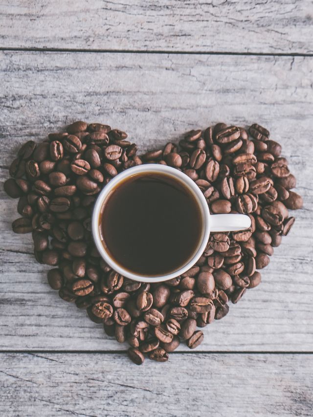 A cup of coffee is surrounded by coffee beans in the shape of a heart.