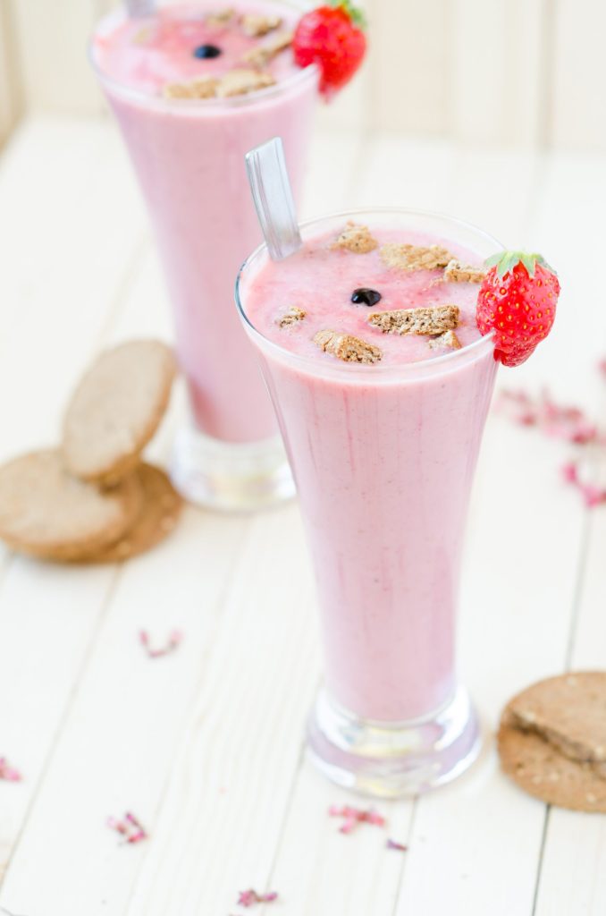 Two glasses of smoothie with strawberries and granola on a wooden table.