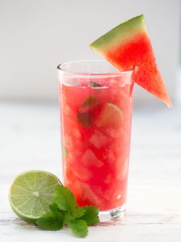 red drink in glass with watermelon, lime, and mint