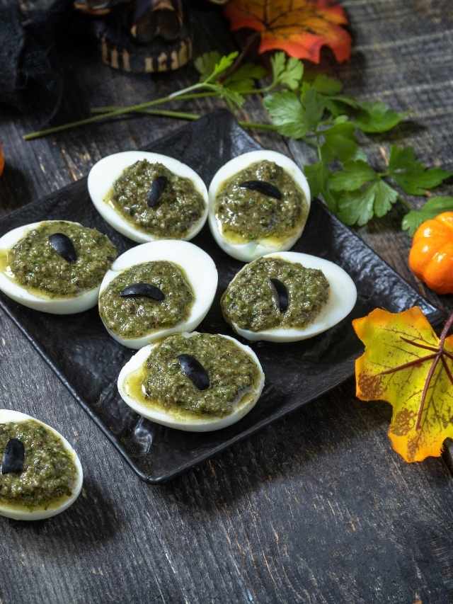Deviled eggs with pesto on a black plate.