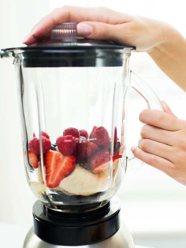 A person holding a blender full of fruit and berries.