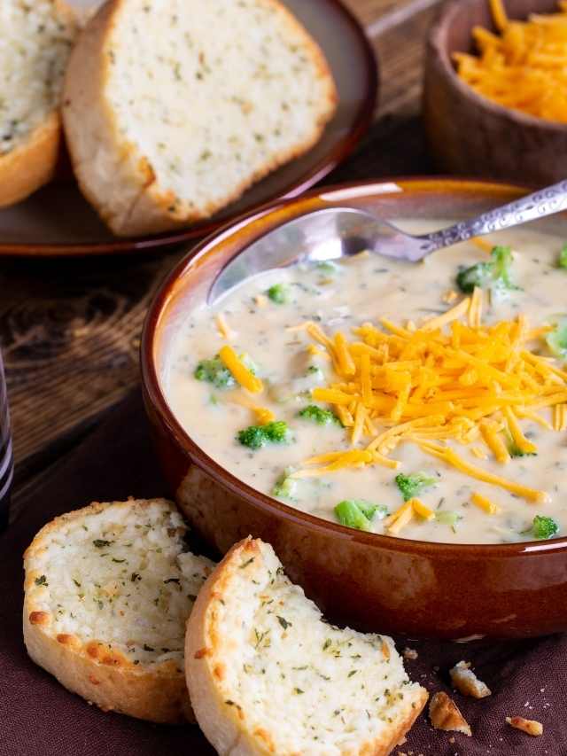 Cheesy broccoli soup in a bowl with bread and cheese.