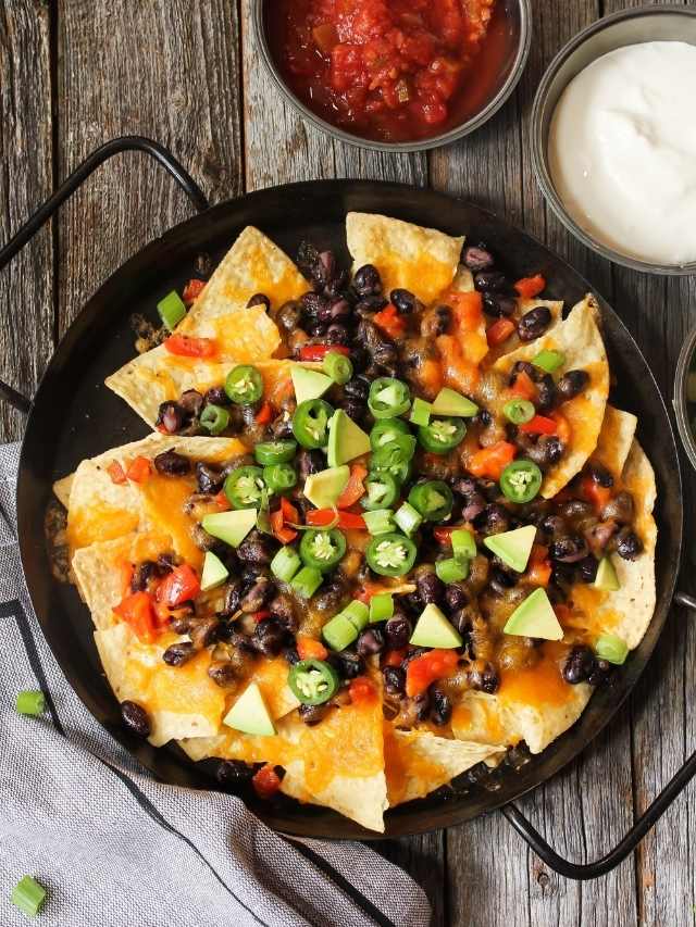 Black bean nachos in a skillet with sour cream and guacamole.