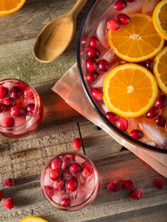 A bowl of cranberry punch with oranges and ice.