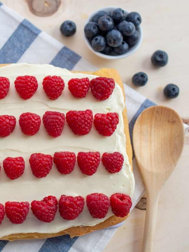 A white cake with raspberries and blueberries on top.