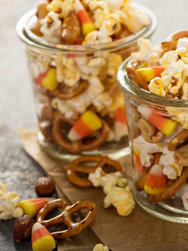 Two jars filled with candy corn, pretzels and popcorn.