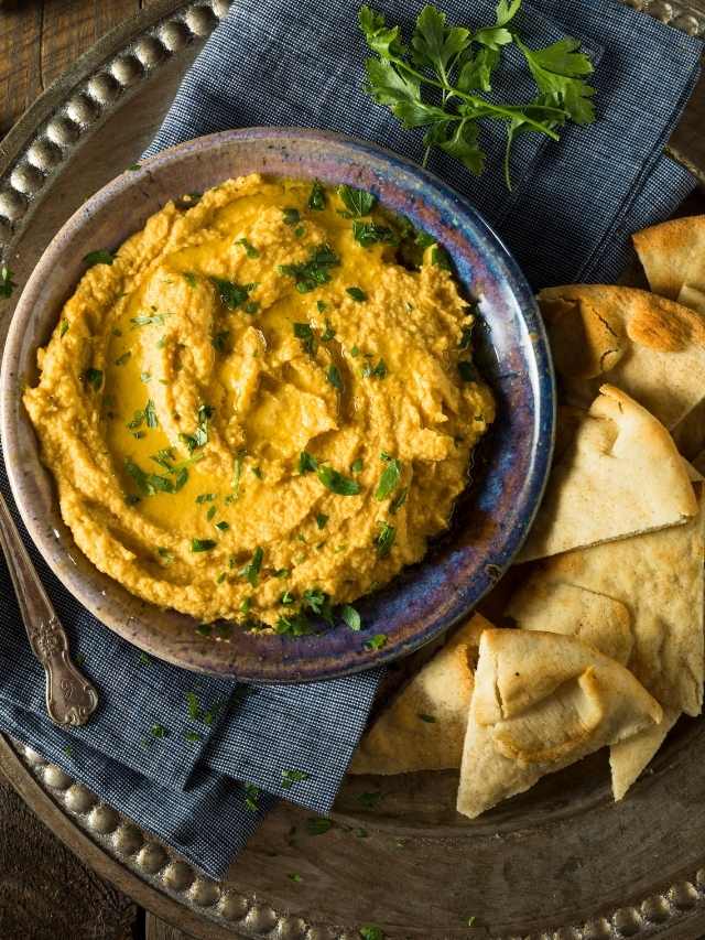 A delicious bowl of hummus topped with a sprinkling of pumpkin seeds, served alongside warm pita bread on a rustic table.