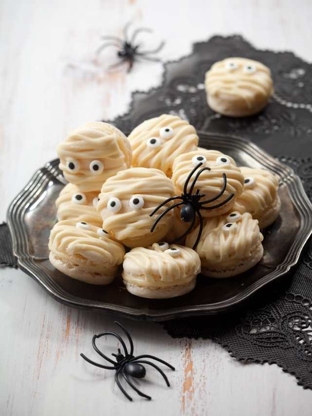 Mummy macarons on a plate with spiders on them.