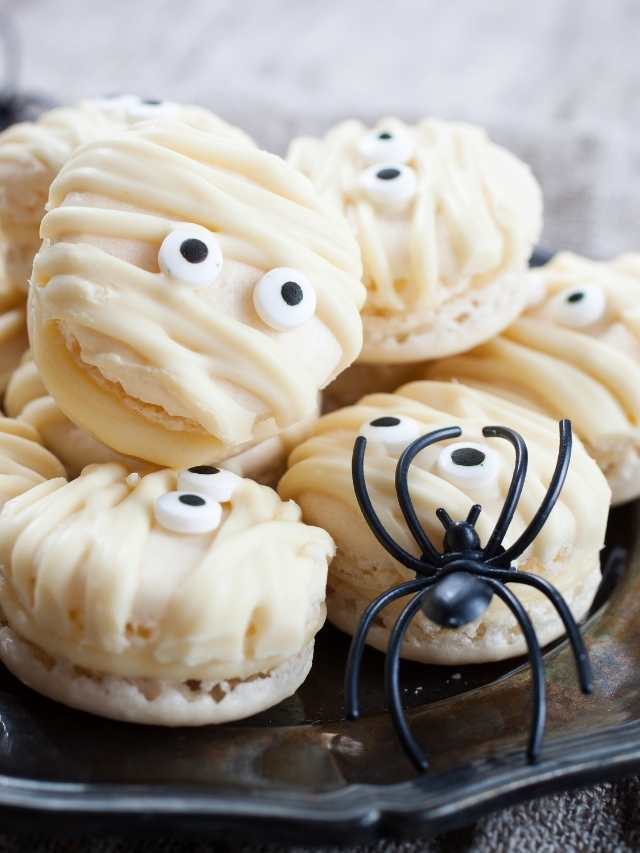 Mummy macarons with eyes and spiders on a plate.