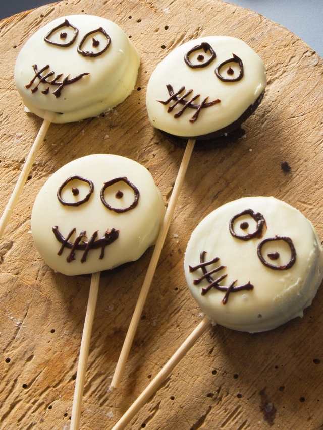 Three chocolate skeleton lollipops on a wooden cutting board.