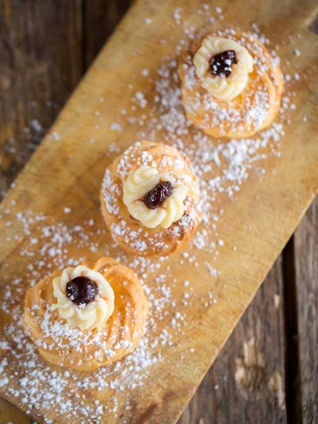 Three pastries with jam and powdered sugar on a wooden cutting board.