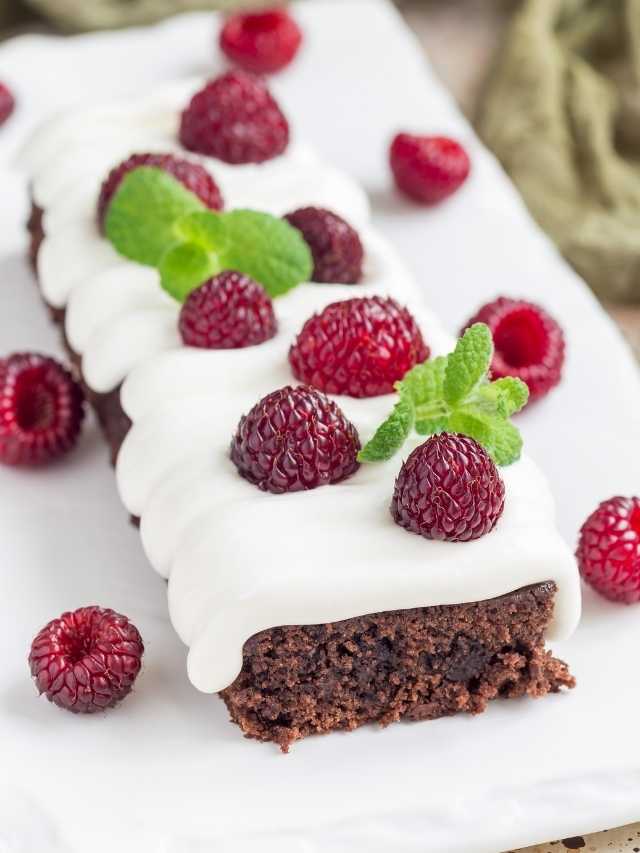 A brownie with cream and raspberries on a white plate.
