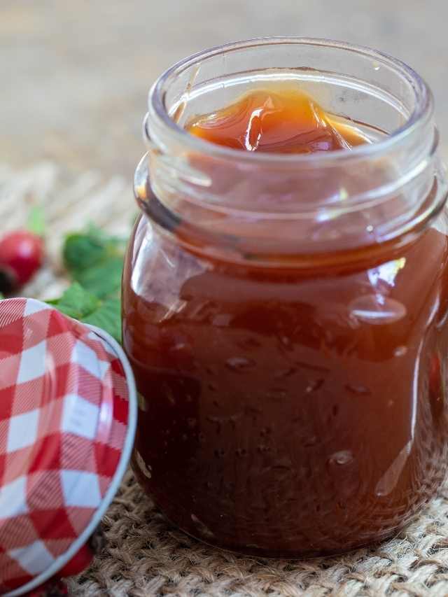 A jar of caramel sauce next to a jar of cranberries.