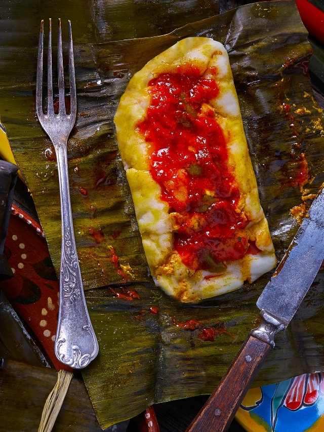 A plate of food on a banana leaf with a knife and fork.