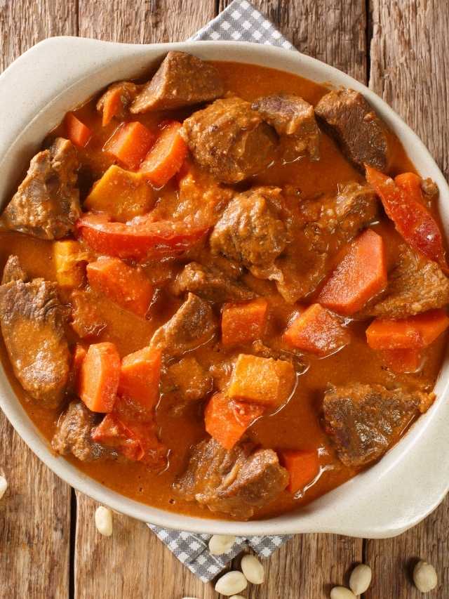 Beef stew with carrots and peanuts on a wooden table.