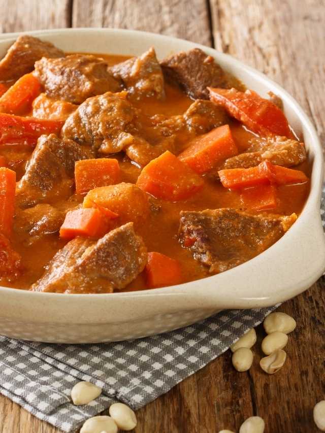 Beef stew in a white bowl with carrots and nuts.
