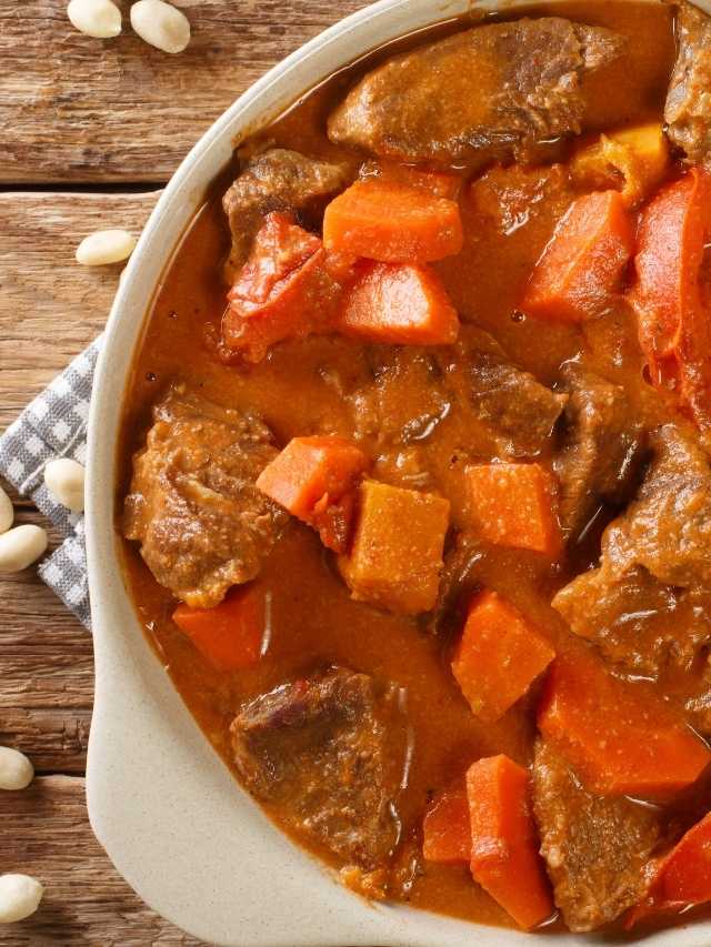 Beef stew in a white bowl with carrots and nuts.