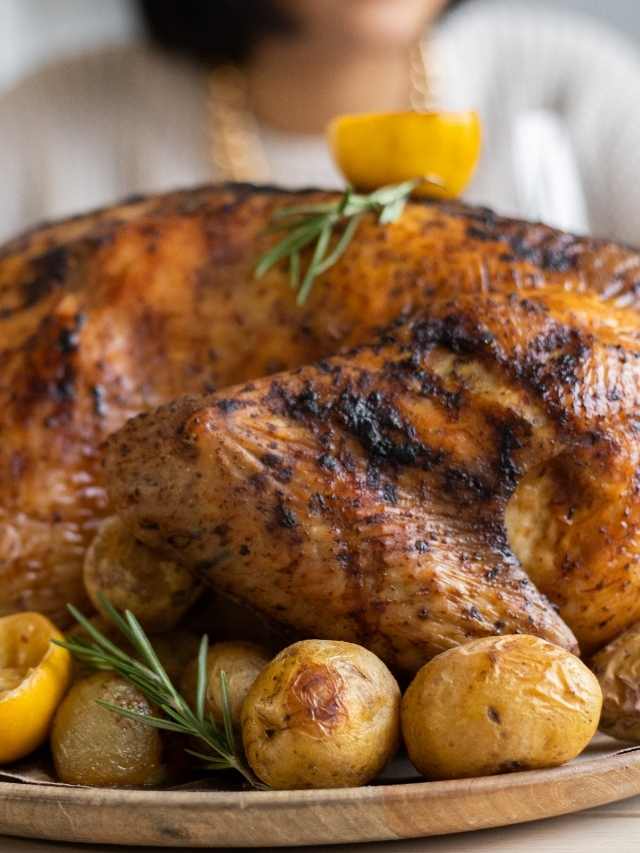 A roasted turkey on a plate with potatoes and lemons.