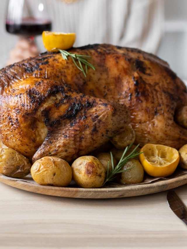 A roasted turkey with potatoes and lemons on a plate.