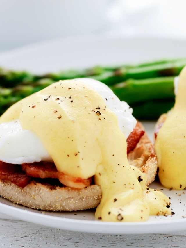 Eggs benedict with bacon and asparagus on a white plate.