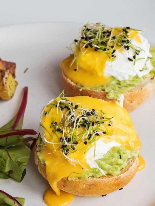 Two eggs benedict with avocado on a plate.