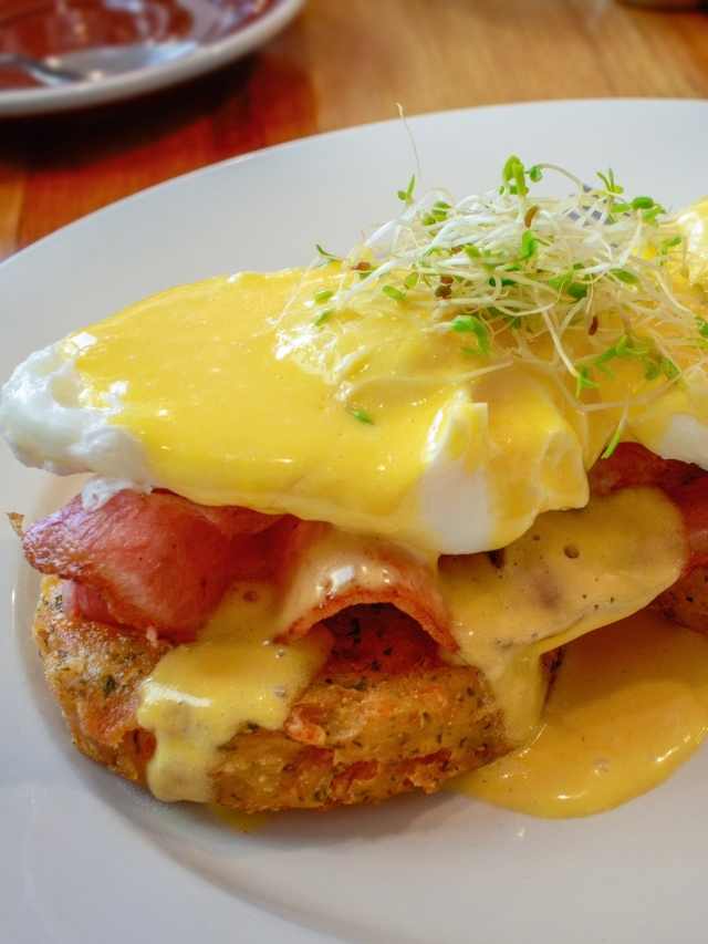 A plate with eggs benedict and bacon on it.