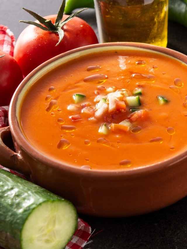 A bowl of tomato soup with cucumbers and tomatoes.