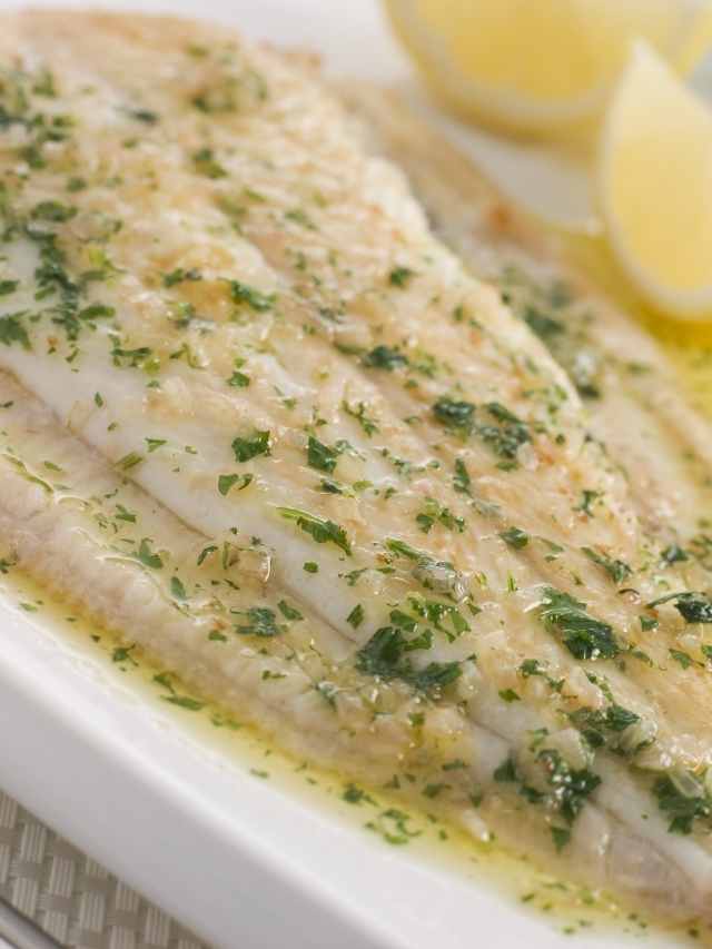 Fish fillet with lemon and herbs on a white plate.