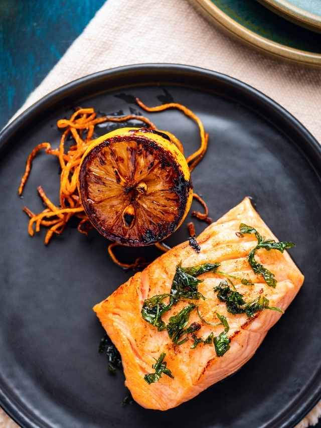 Grilled salmon on a black plate with lemon slices.