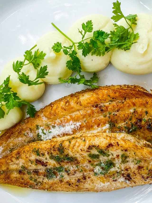 Fish fillets with potatoes and herbs on a white plate.