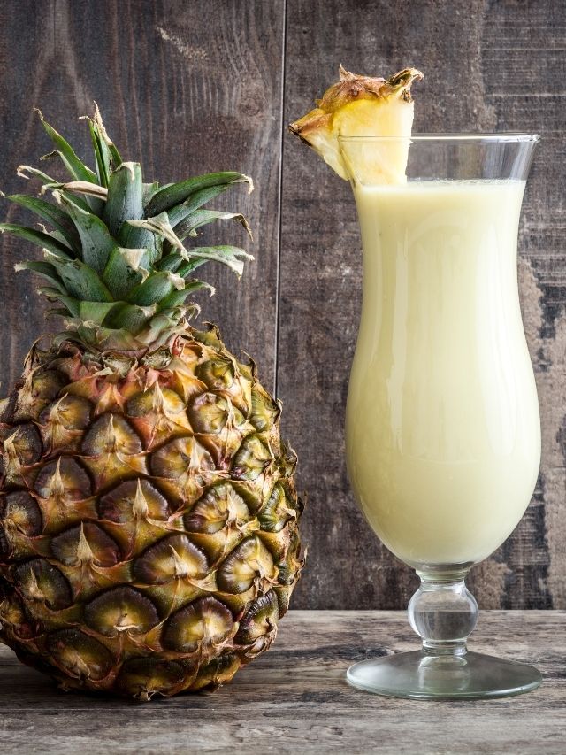 A refreshing glass of pineapple juice and a whole pineapple resting on a rustic wooden table.