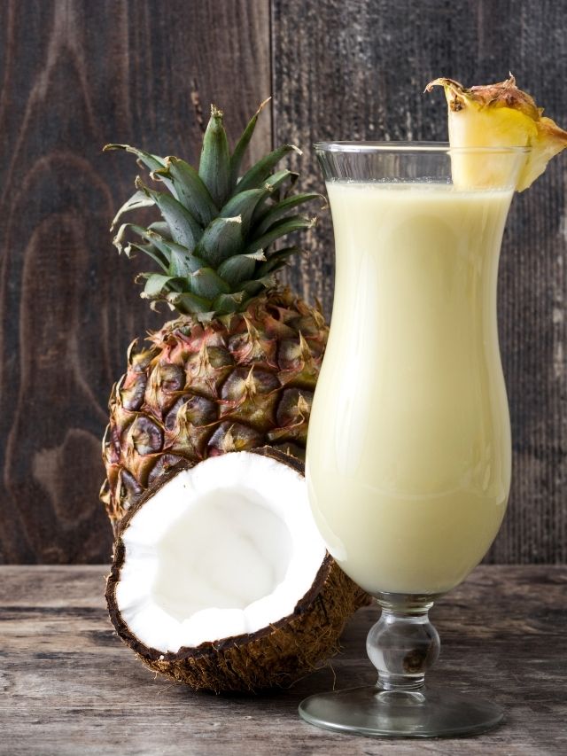 A goya pina colada recipe featuring a pineapple and a coconut on a wooden table.